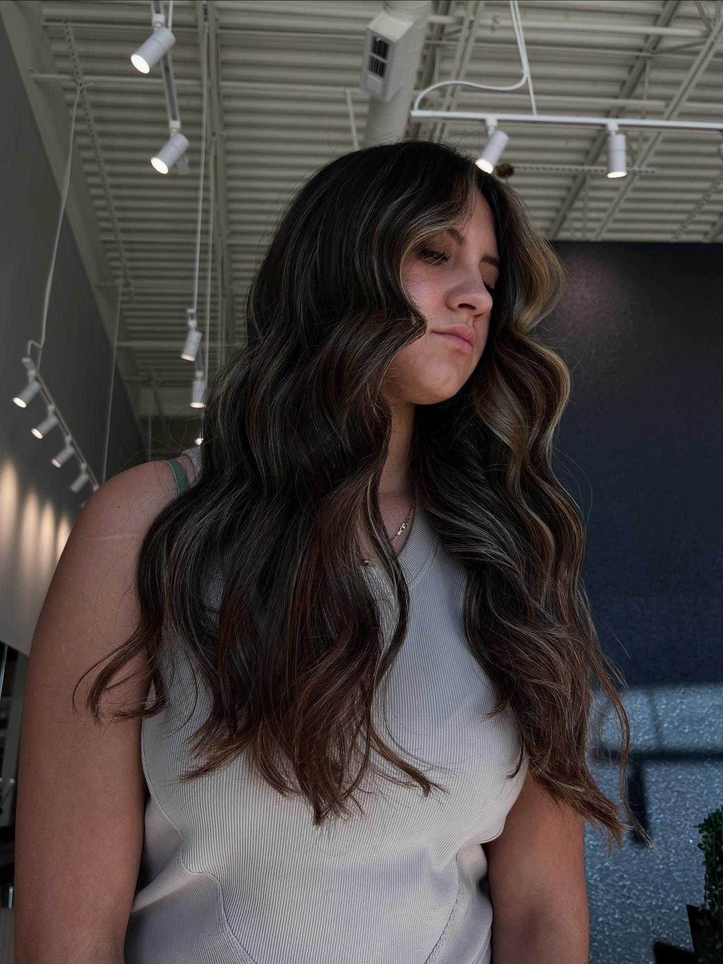 Young woman with long, wavy hair, standing in a modern, well-lit interior space.