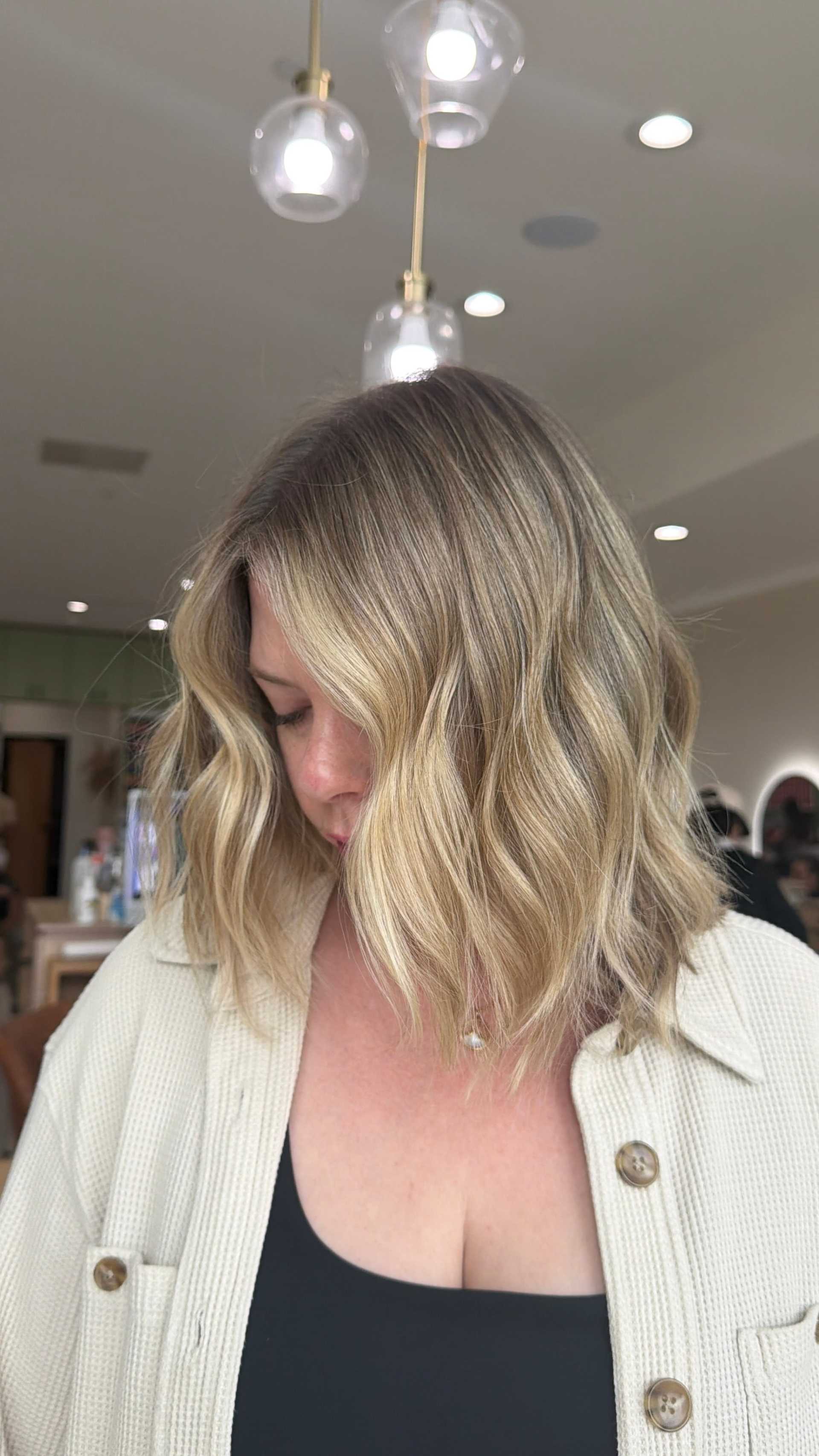 Woman with wavy blonde hair in a salon, wearing a beige shirt.