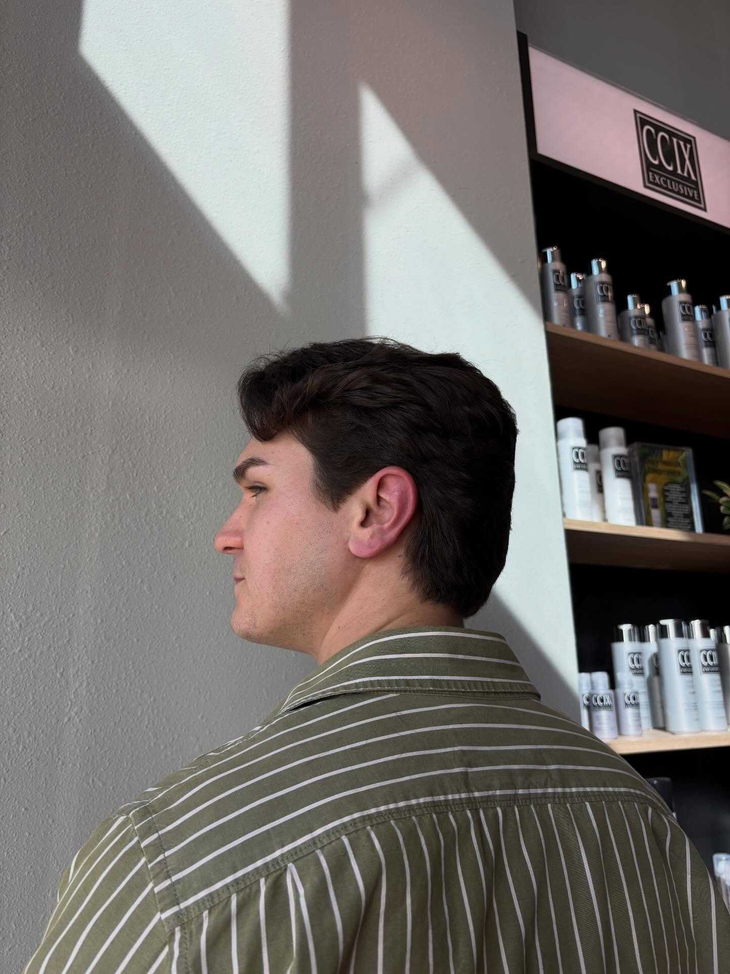 Man with dark hair in a striped shirt standing by shelves of hair products.