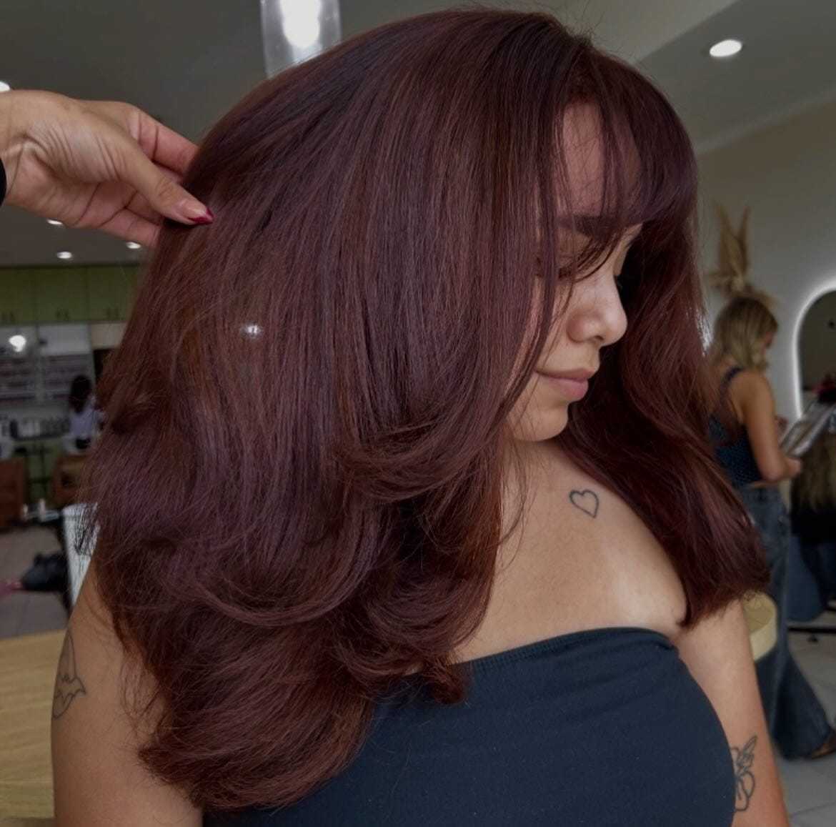 Woman with voluminous, deep auburn hair styled, wearing a black top in a salon setting.