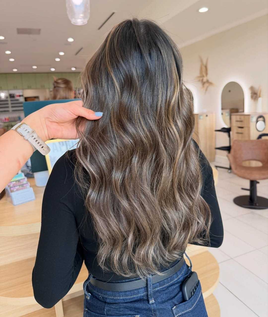 Long wavy hair with ash brown highlights in a salon setting.