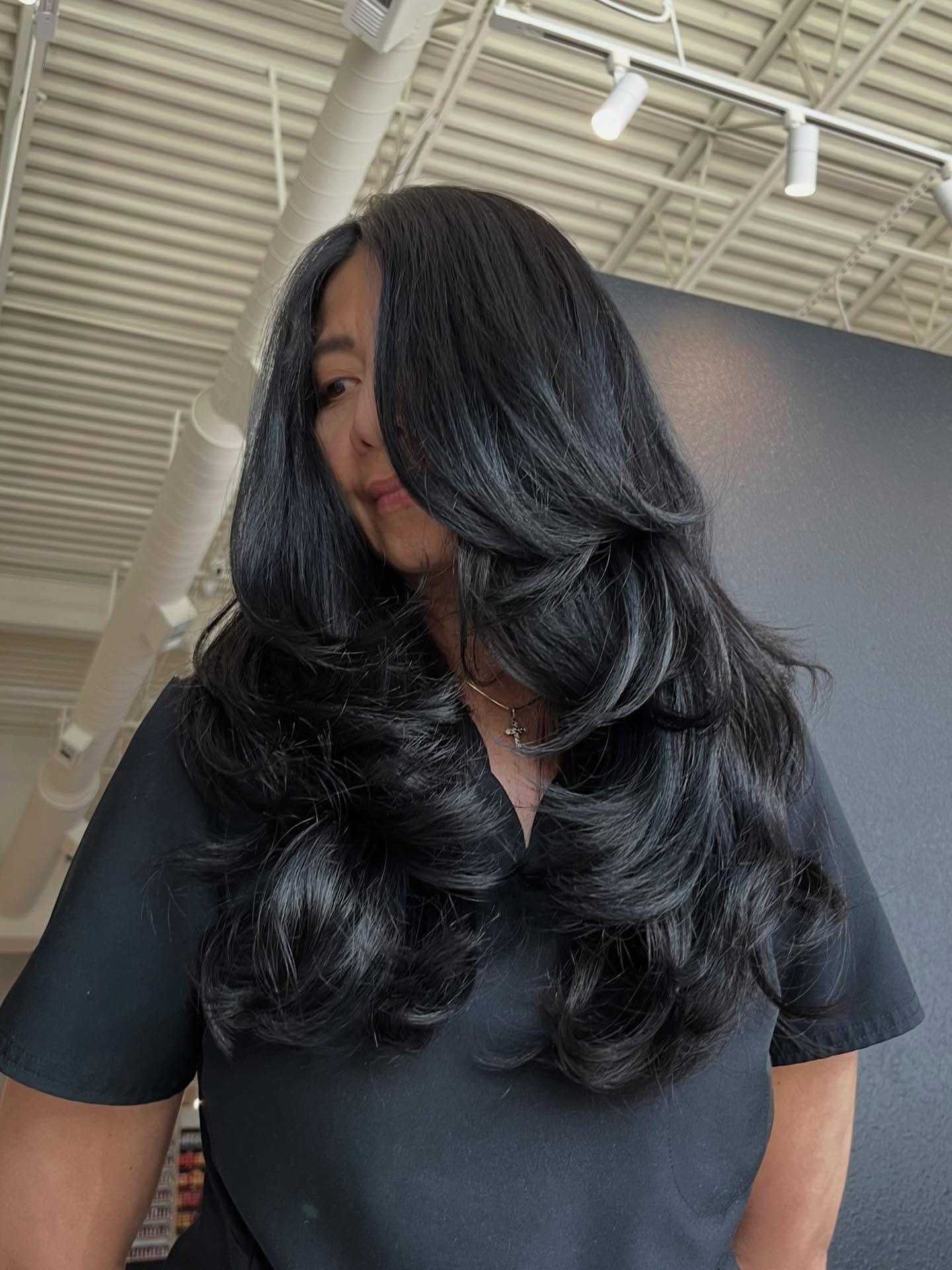 Woman with long, layered black hair in a salon setting.