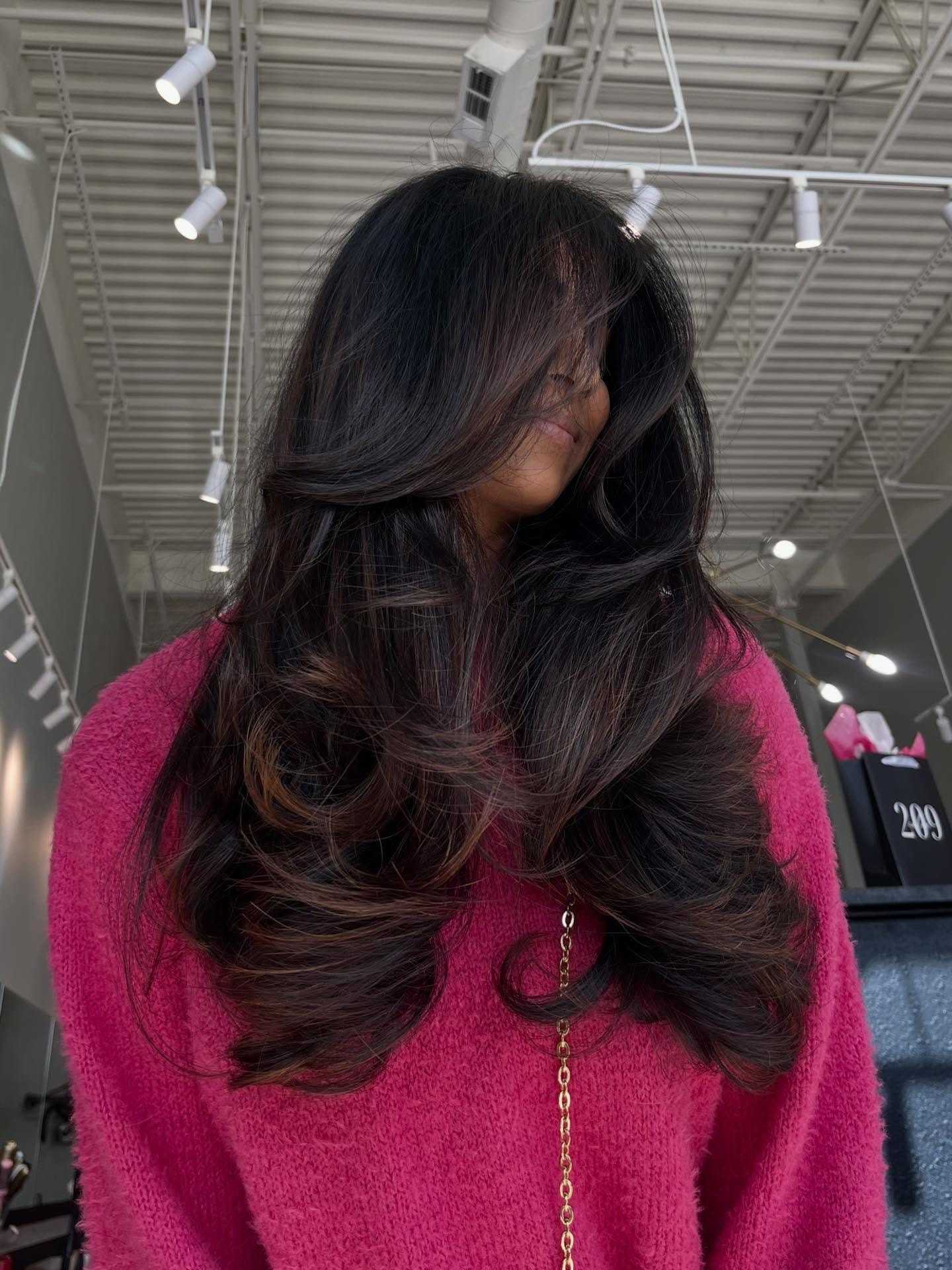 Woman with long, styled hair in a pink sweater at a salon.